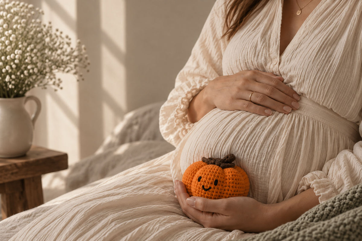 Pregnant woman in a cream dress holding a smiling crocheted pumpkin against her bump